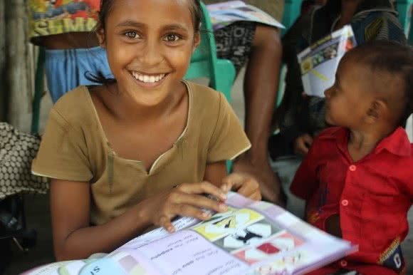 Children from Liquica reading the Lafaek Community Magazine during one of CARE’s Health Program Mother’s Group meetings