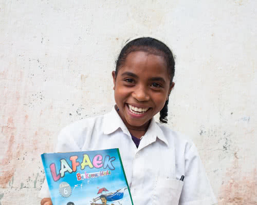 A girl smiles happily holding her schoolbook.