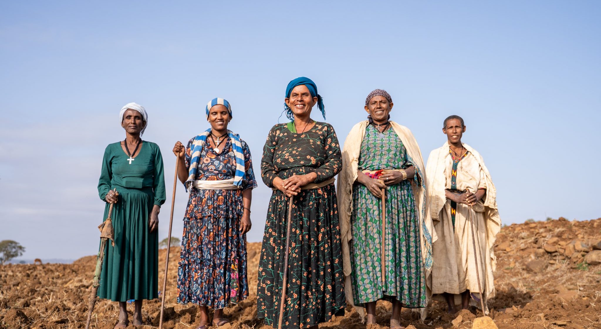 Five women stand together with their tools on a ploughed field in Amhara Region. Working as a group, women are taking a visible role in preparing land and restoring soils for more climate-resilient farming.